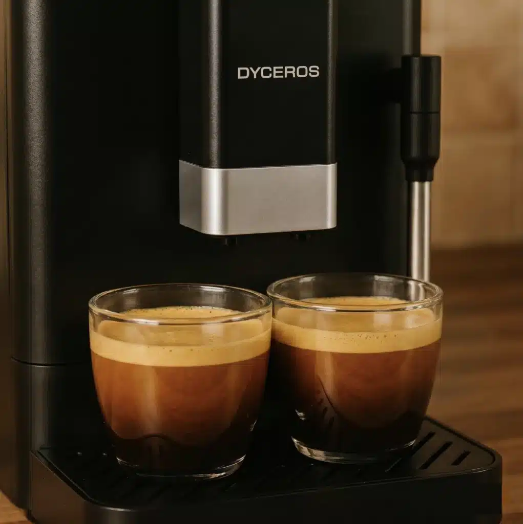 Dyceros Deux tasses en verre remplies d'espresso sont posées sur le plateau d'égouttage d'une machine à café DYCEROS, chacune étant recouverte d'une épaisse couche de crème.