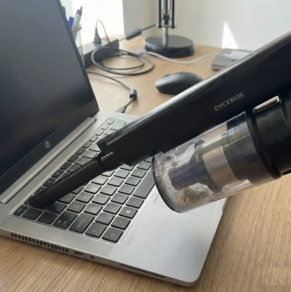 Dyceros Un aspirateur à main est utilisé pour nettoyer le clavier d'un ordinateur portable sur un bureau en bois avec des fournitures de bureau en arrière-plan.