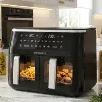 Dyceros La friteuse Dyceros ClearFry Duo 9L (2x4,5L, 2800W) présente un design noir, des compartiments doubles avec des fenêtres transparentes pour cuire des frites et du poulet ensemble, et un affichage numérique avec des réglages de température séparés sur un comptoir de cuisine blanc.