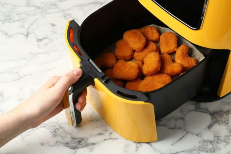 Dyceros Une main sort le panier d'une friteuse jaune remplie de nuggets de poulet dorés sur un comptoir en marbre.