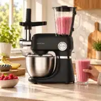 RC800_smoothie Dyceros Un robot de cuisine multifonction noir, équipé d'un mixeur et d'un hachoir à viande, posé sur un plan de travail à côté d'une main tenant un verre de smoothie rose.